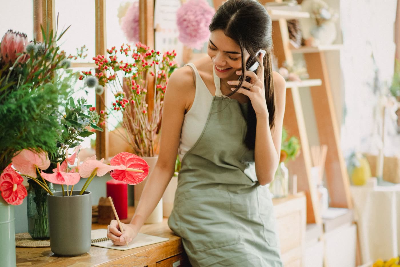 A florist taking a customer's call and writing notes at her shop counter