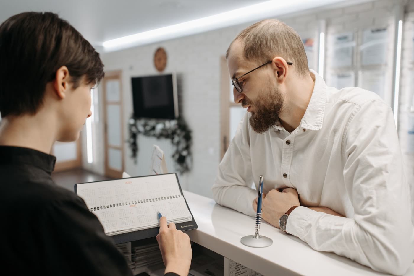 A receptionist showing a patient open appointment times at a clinic front desk