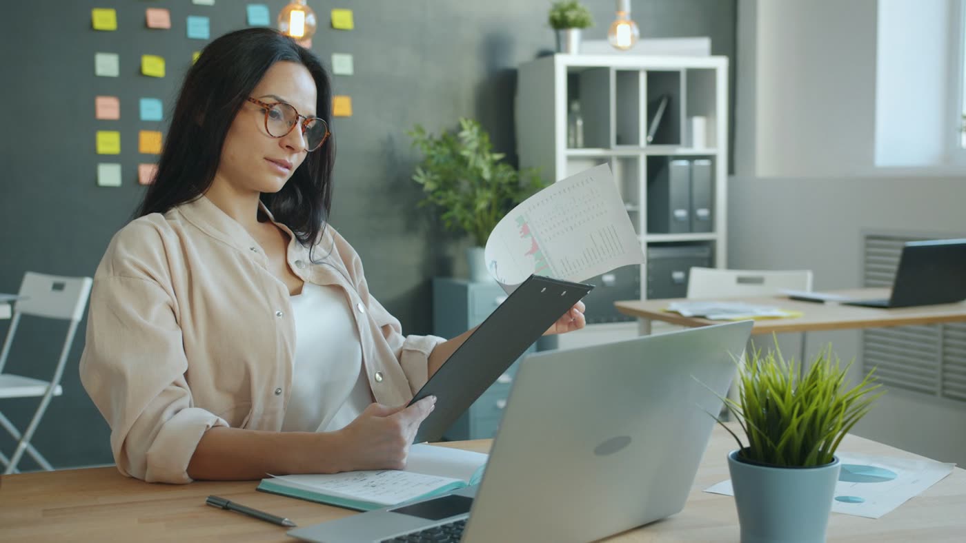 An office manager reviewing intake paperwork at a desk beside a laptop